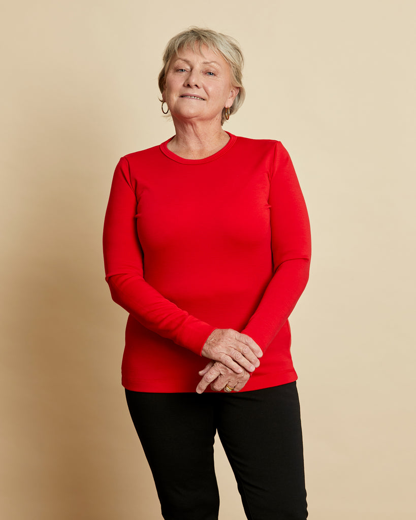 Woman wearing soft Australian Merino wool long sleeve crew neck in tomato red. Designed to wear next to the skin either as a base layer or as a t.shirt style on its own. This style is perfect for layering. Made in Australia at Woolerina's workrooms at Forbes in central west NSW.